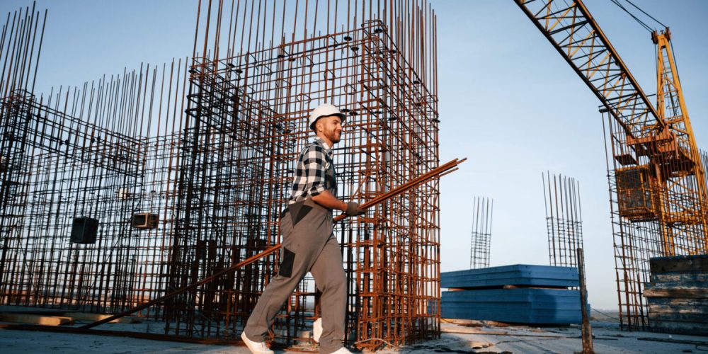 Near big metal objects. Man is working on the construction site at daytime.